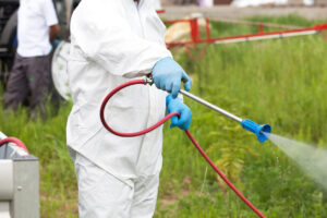 Person in protective suit spraying chemicals or pesticides in grassy area