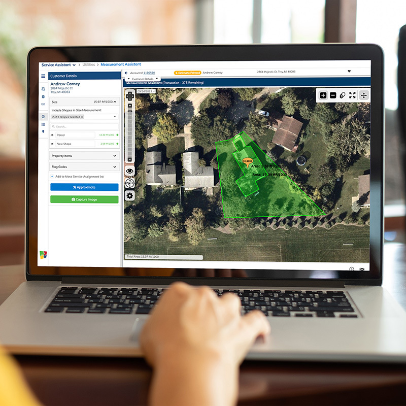 Laptop screen displaying property mapping software with aerial view of houses