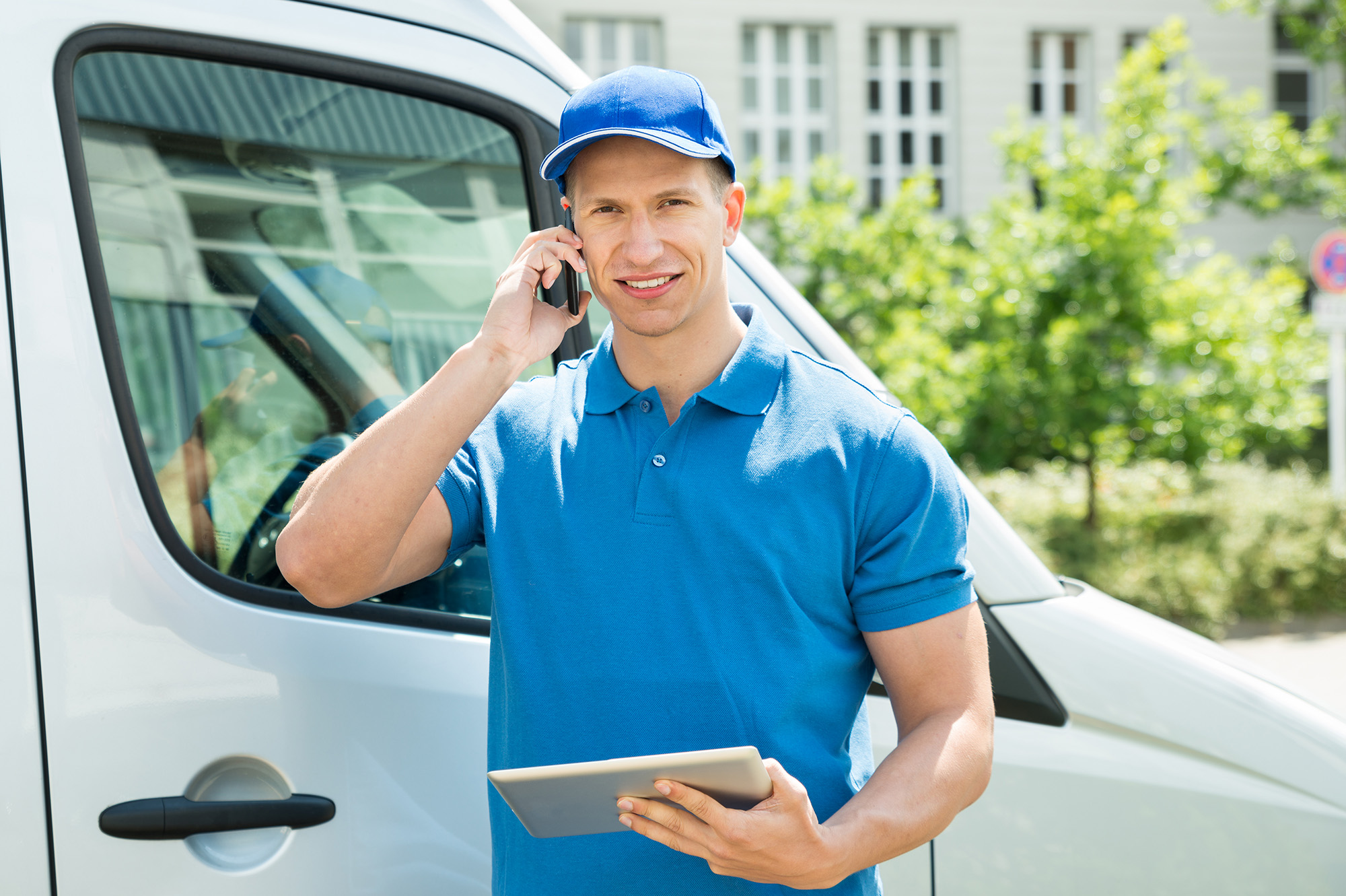 Delivery worker in blue uniform talking on phone next to white van