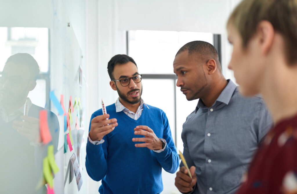 Business professionals discussing project with sticky notes on glass wall