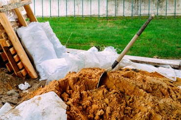 Construction site with shovel, dirt pile, and white bags on green lawn