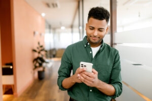 Person in green shirt using smartphone in modern office hallway