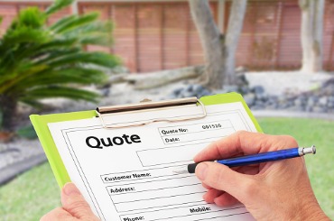 Hand filling out a quote form with blue pen, green clipboard, outdoor setting