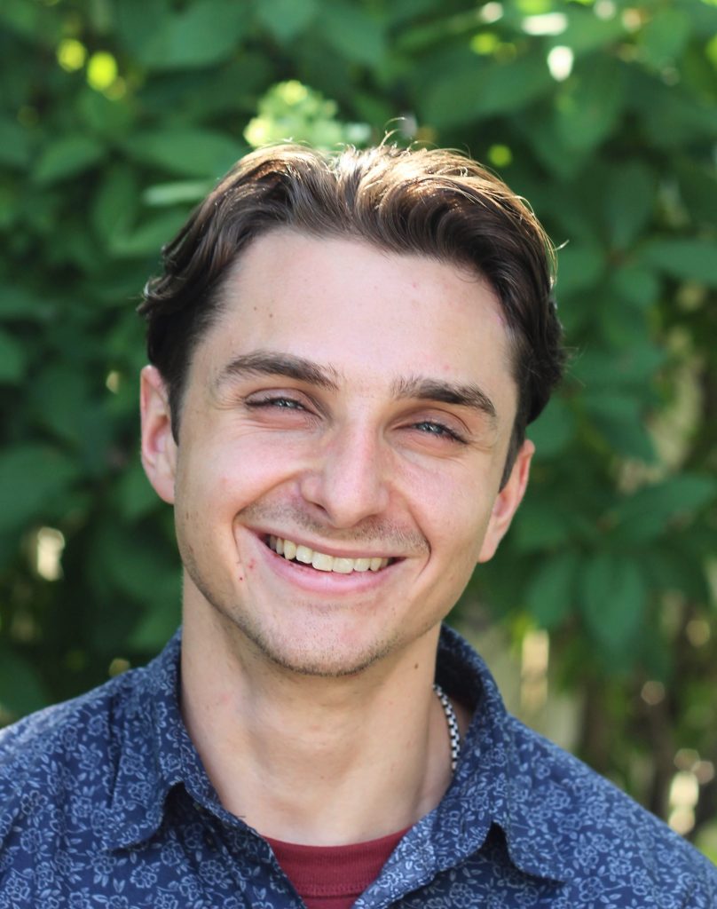 Person smiling warmly with green foliage in background