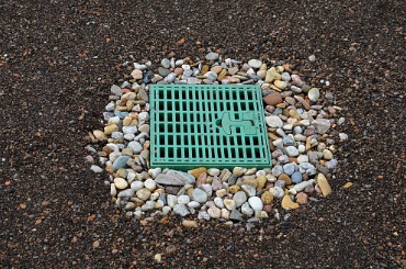 Green drainage grate surrounded by colorful stones on dark ground