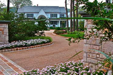Elegant home with curved driveway, stone walls, and colorful flower beds