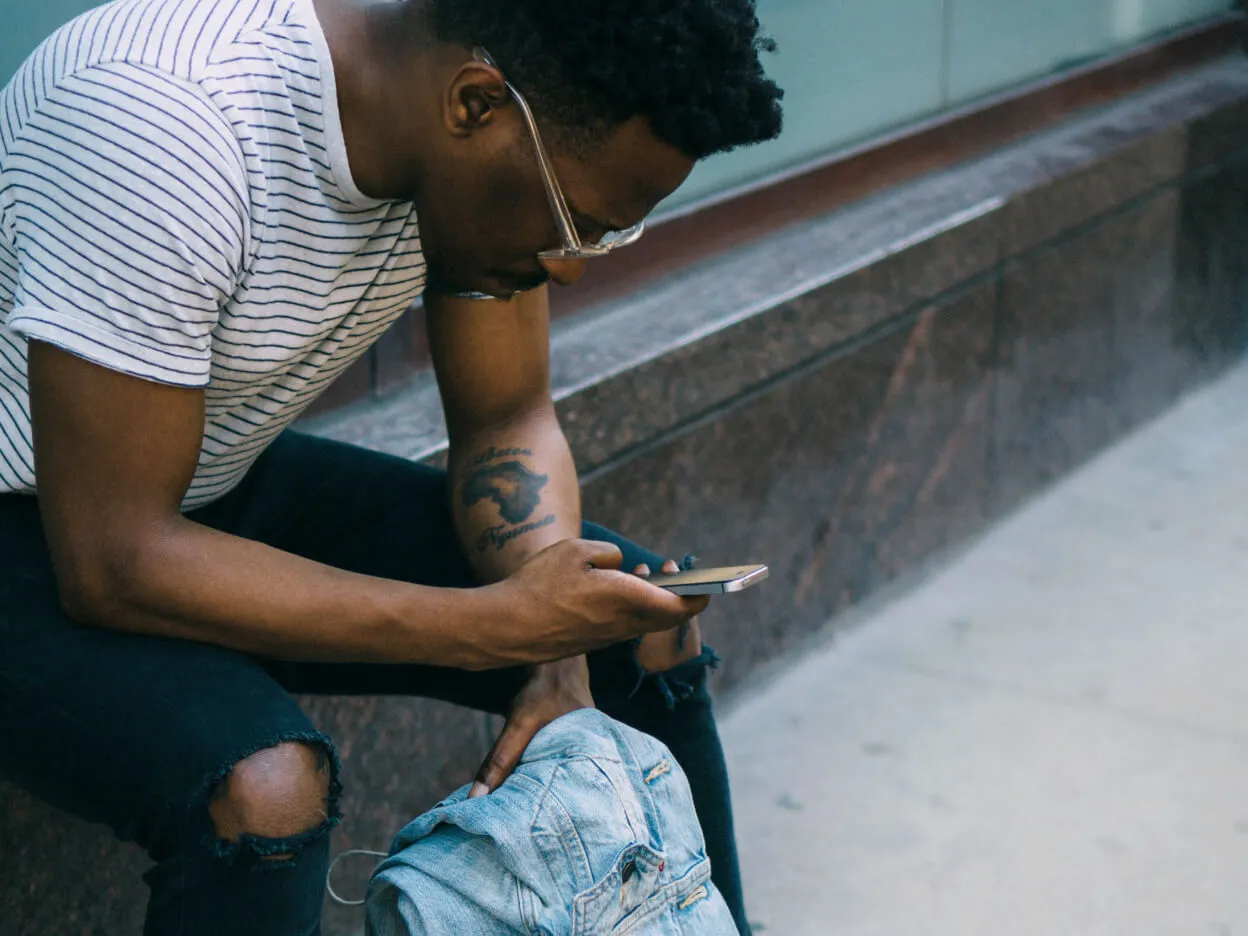 A man sitting whilst looking down into his phone