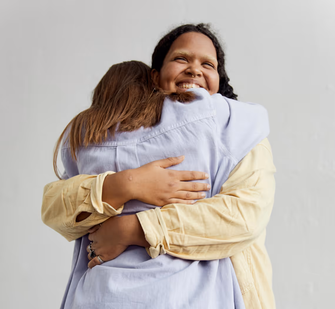 Two women warmly hugging each other, one smiling with eyes closed.