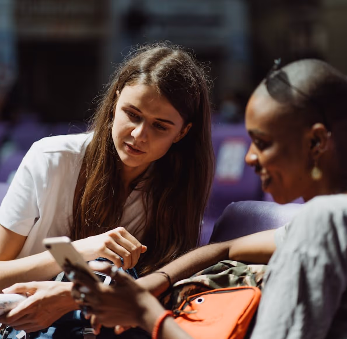 Two women sitting close together looking at a smartphone, engaged in conversation.