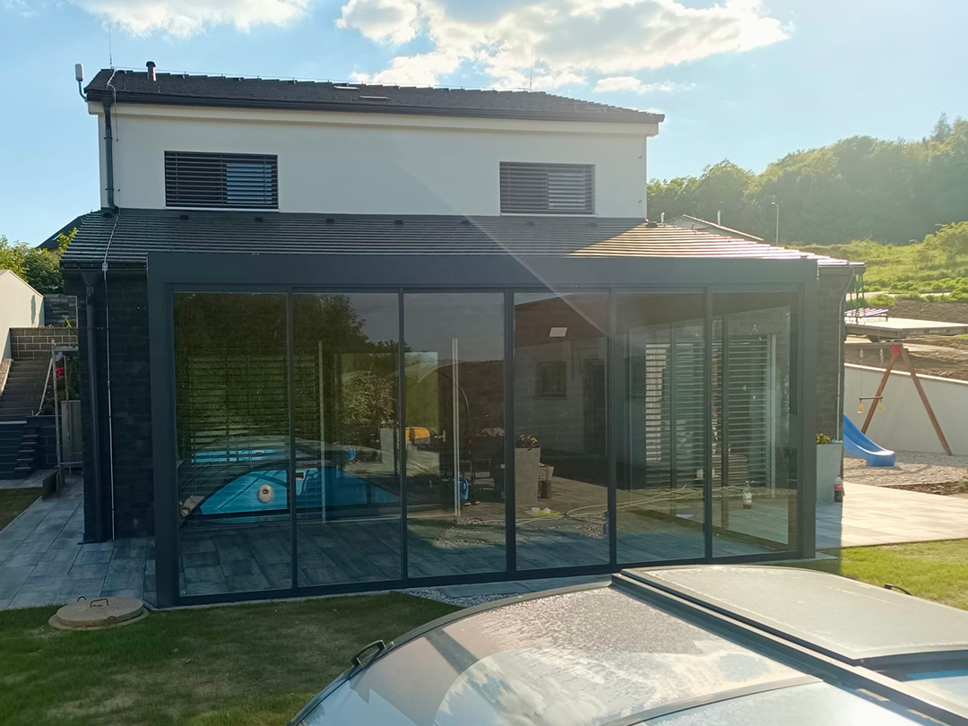 Zasklená terasa pri dome s tmavou fasádou a dlažbou – vplyv materiálov na prehrievanie terasy