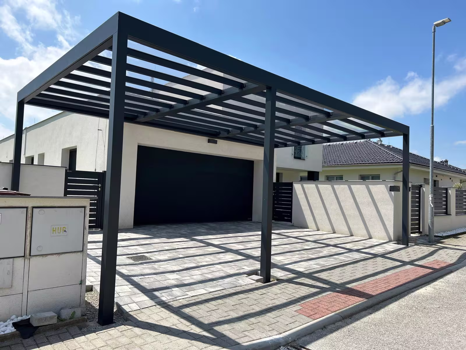 Hliníkový carport s polykarbonátovou střechou před garážovými vraty