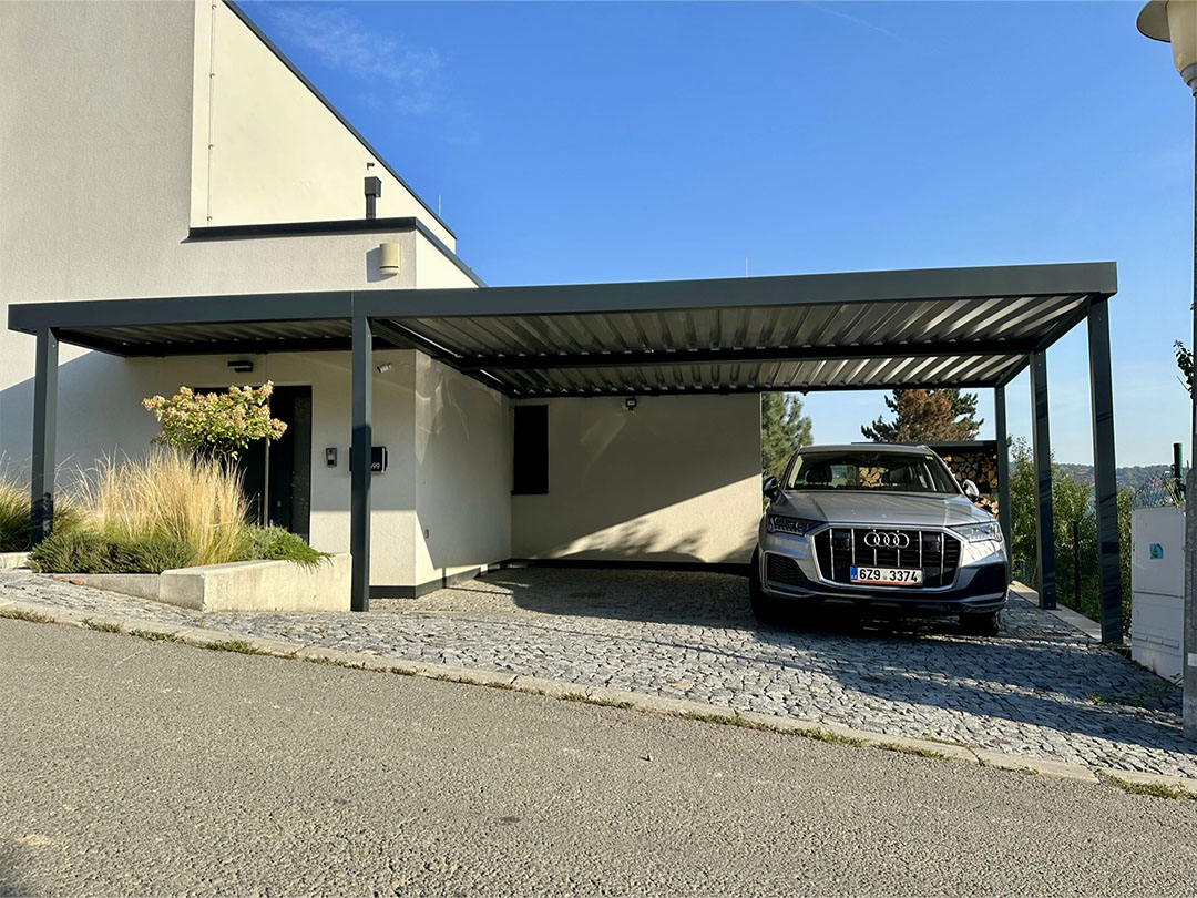Antracitový přístřešek na auto přistavěný k bílému domu, pod ním SUV