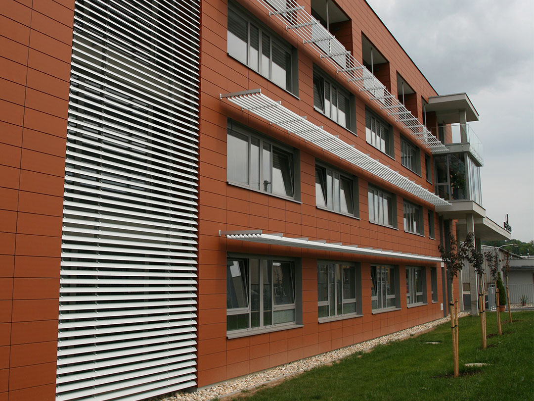Administrativní budova s hliníkovými slunolamy nad okny a vertikálními lamelami na nároží