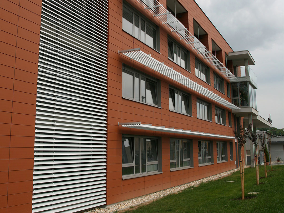 Hliníkové slunolamy nad okny administrativní budovy s oranžovou fasádou