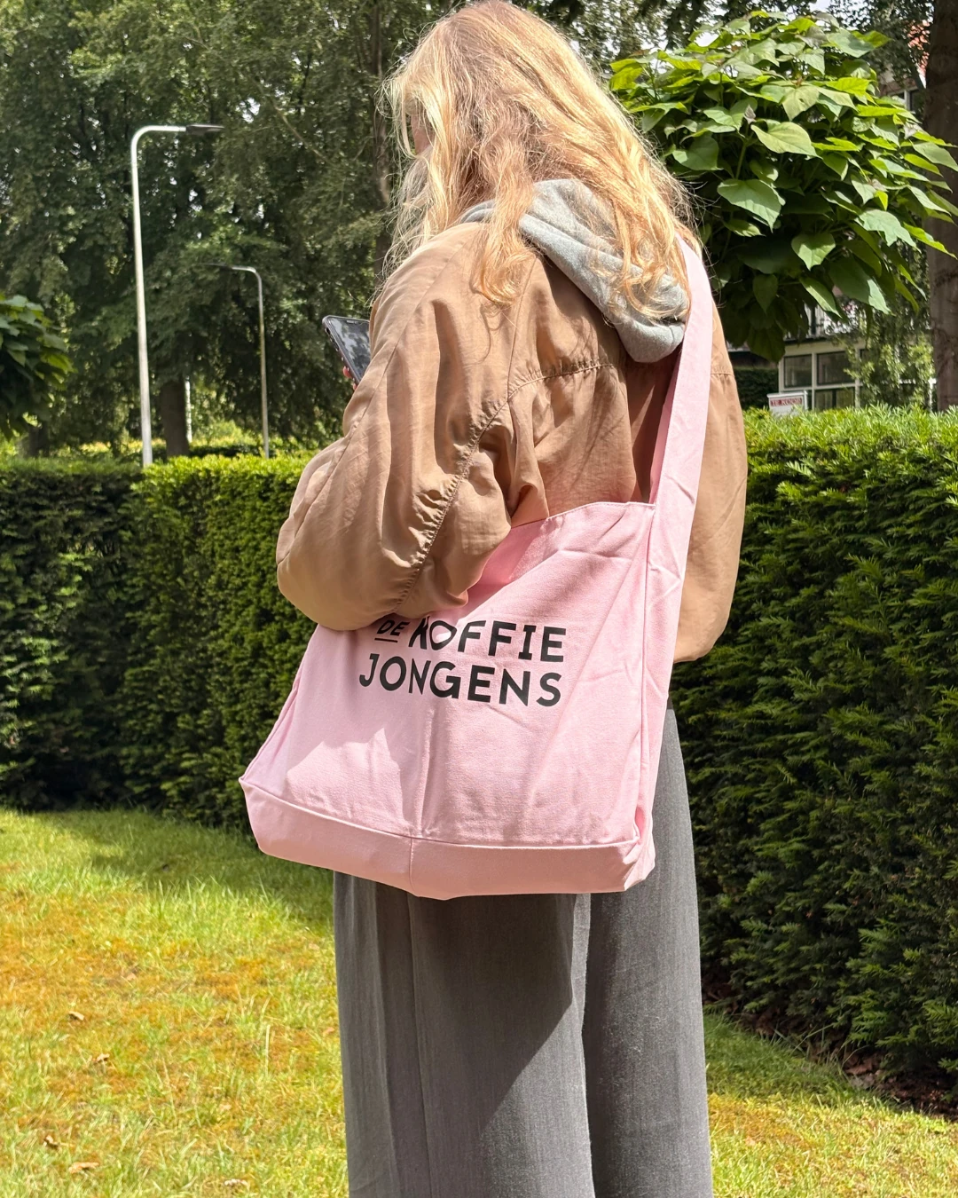 Vrouw loopt buiten met de roze tote tas van De Koffiejongens losjes over de schouder.