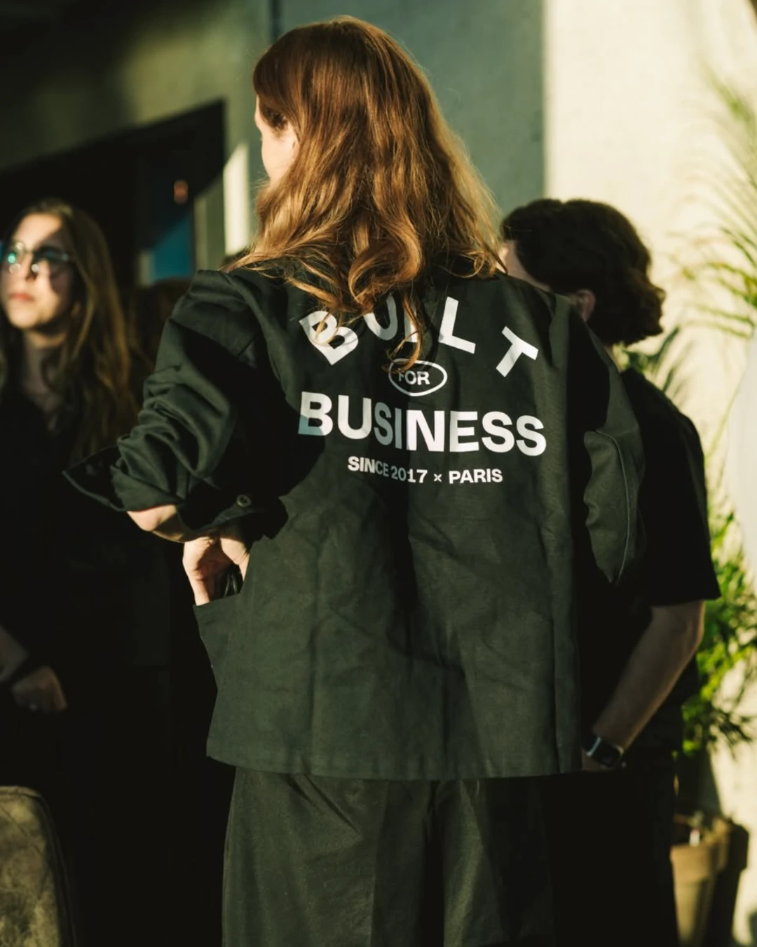Vrouw draagt de donkergroene "Built for Business"-jas van Qonto en Custom95, met uitzicht over Amsterdam op de achtergrond