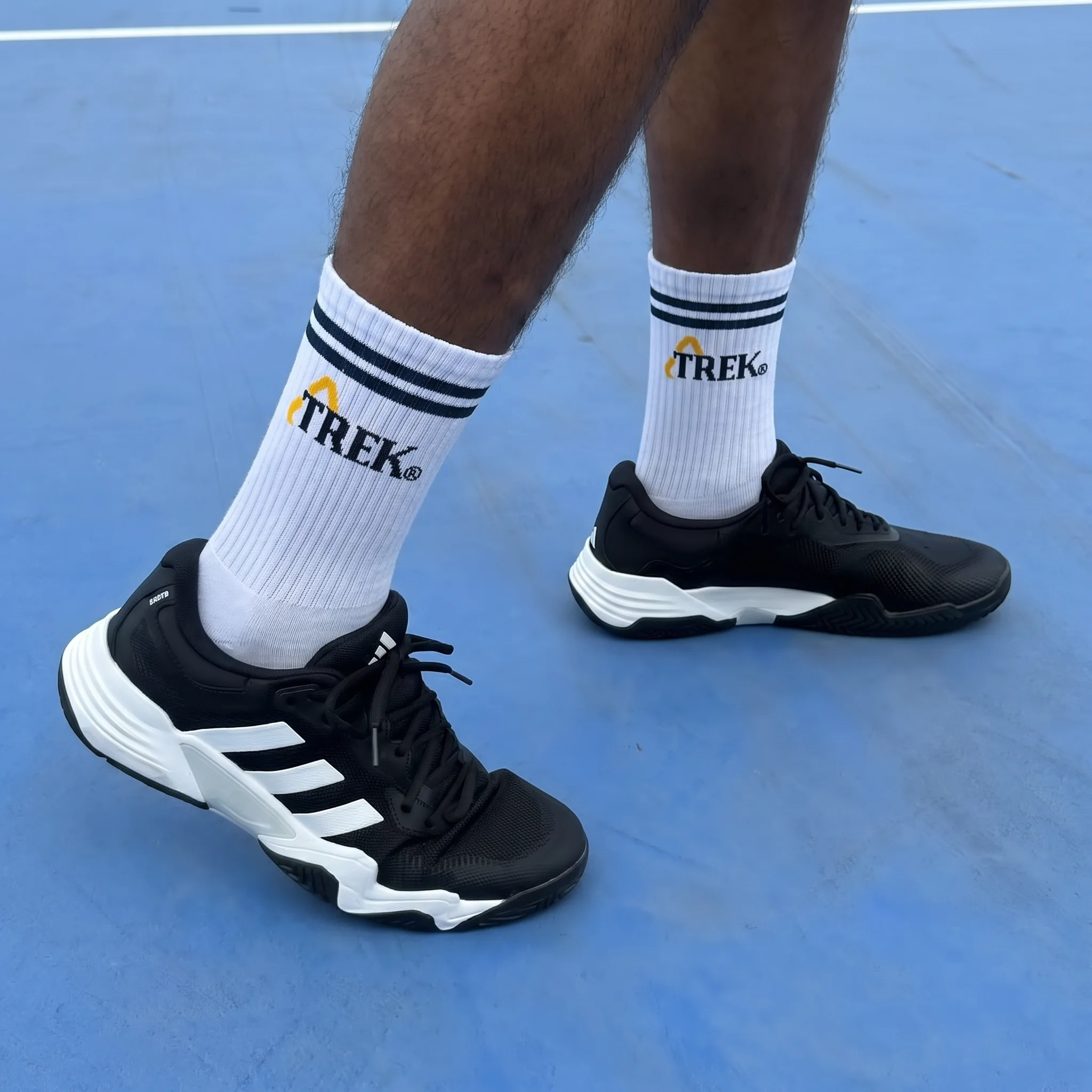 Witte tennissokken met Trek-logo op een blauwe tennisbaan