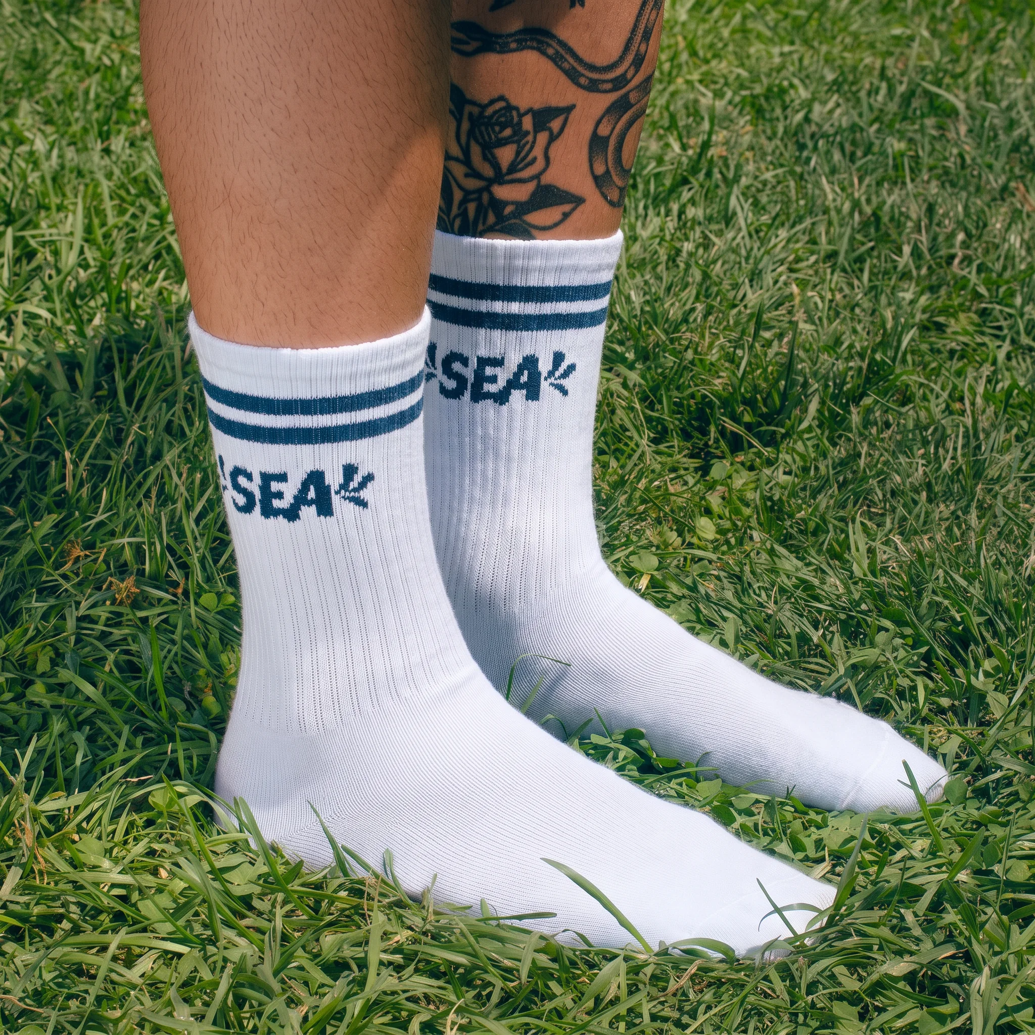 Witte sportsokken met blauwe strepen en SEA-logo in het gras
