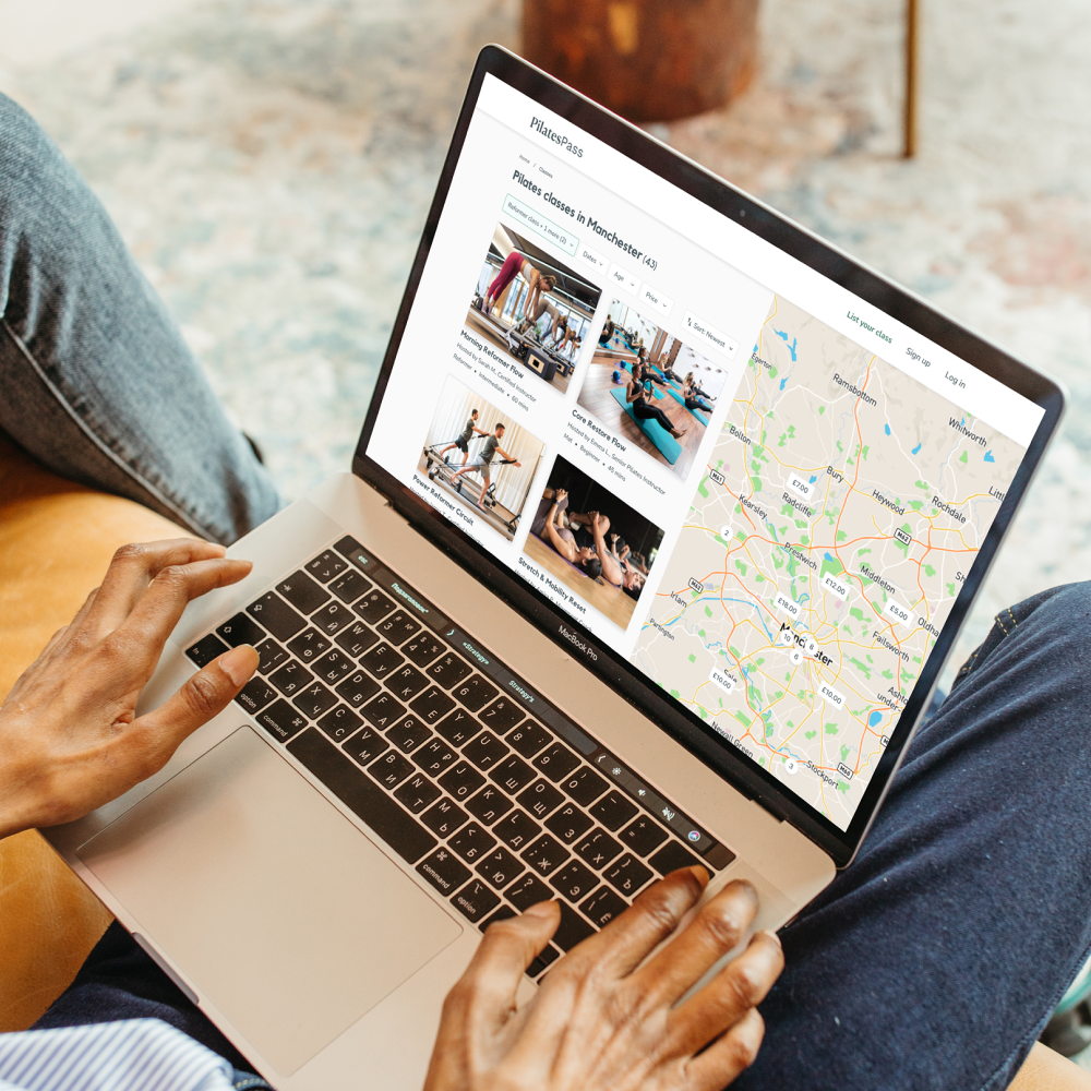 Photograph of someone using a macbook. The screen shows homepage for PilatesPass.