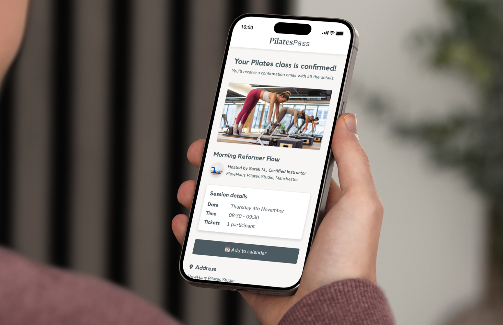 Photograph of someone holding a mobile phone. The screen shows the booking confirmed page for PilatesPass