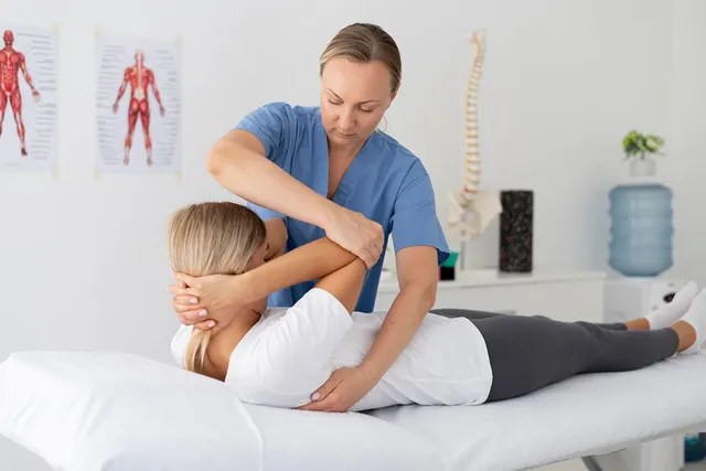 Physiotherapist guiding a female patient through a shoulder and arm mobility stretch during treatment.