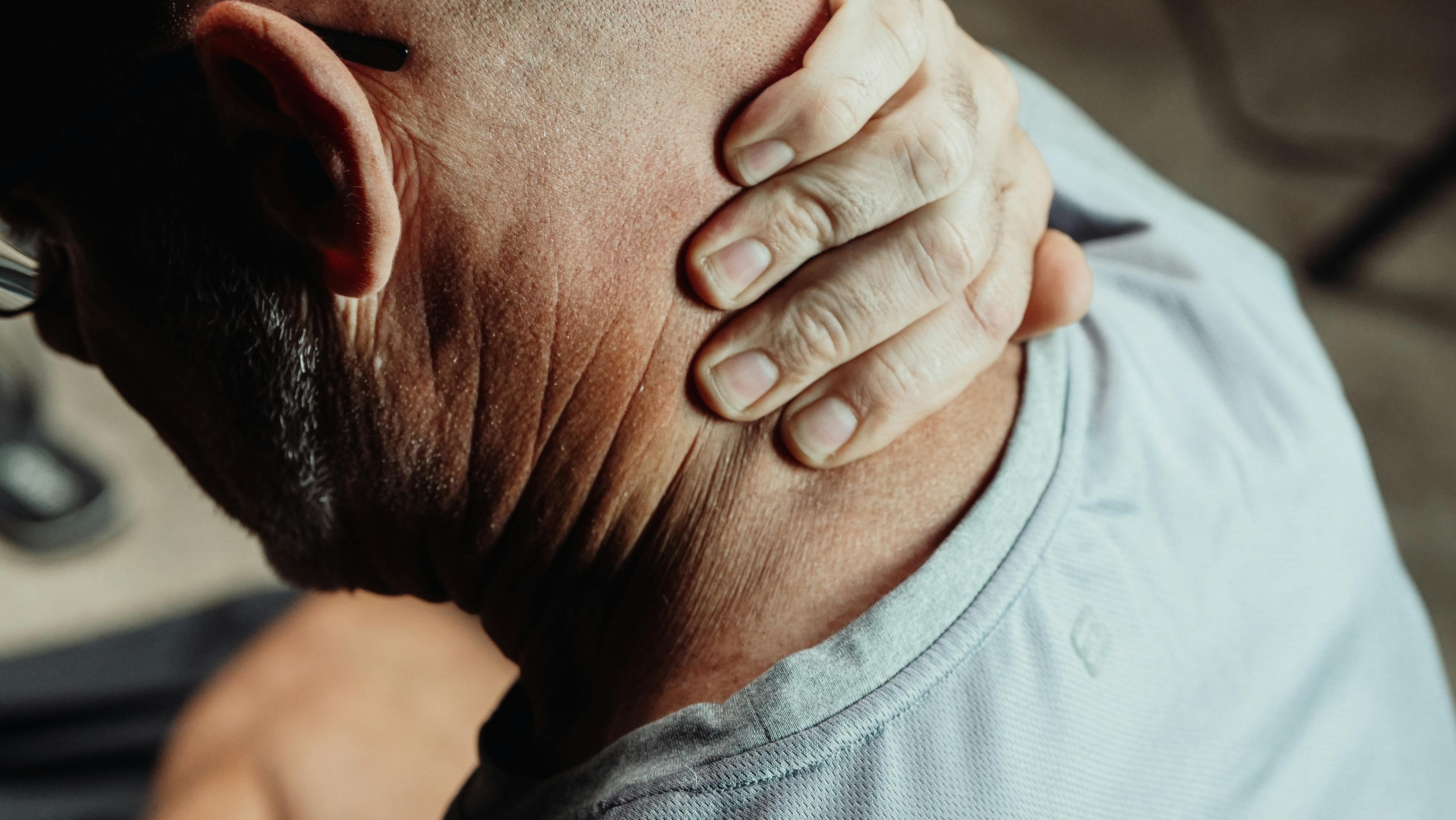 Man experiencing neck pain, holding the back of his neck while seated