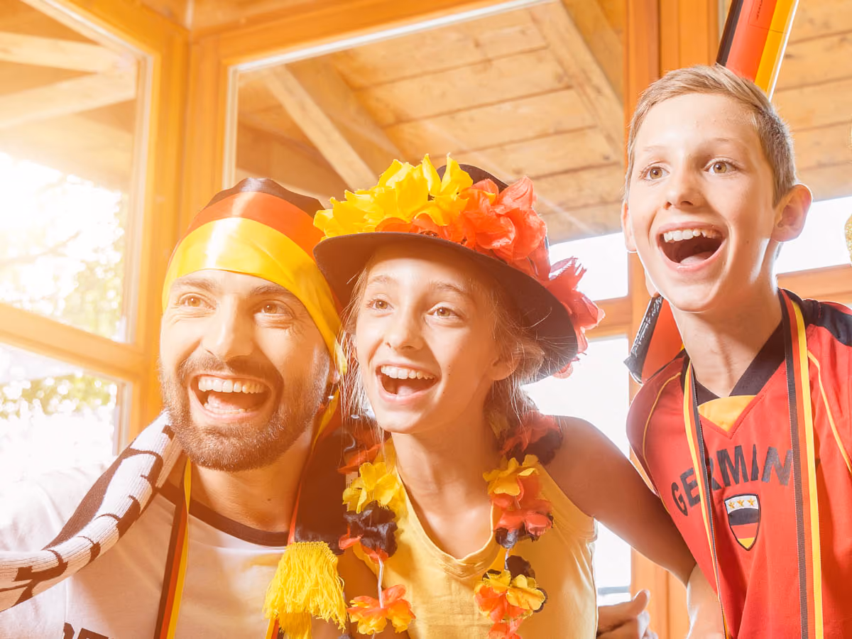 Drei Fußballfans in Deutschland-Fanbekleidung verfolgen begeistert eine Spielübertragung.
