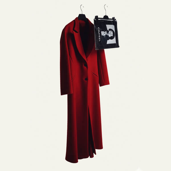 Long red coat with lapels hanging on a black hanger next to a smaller black hanger holding a black and white Chanel shopping bag.