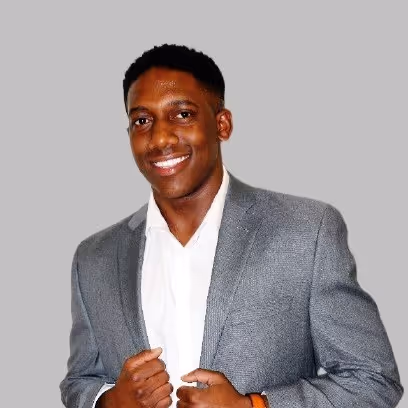 Smiling young man wearing a gray blazer and white shirt against a plain gray background.
