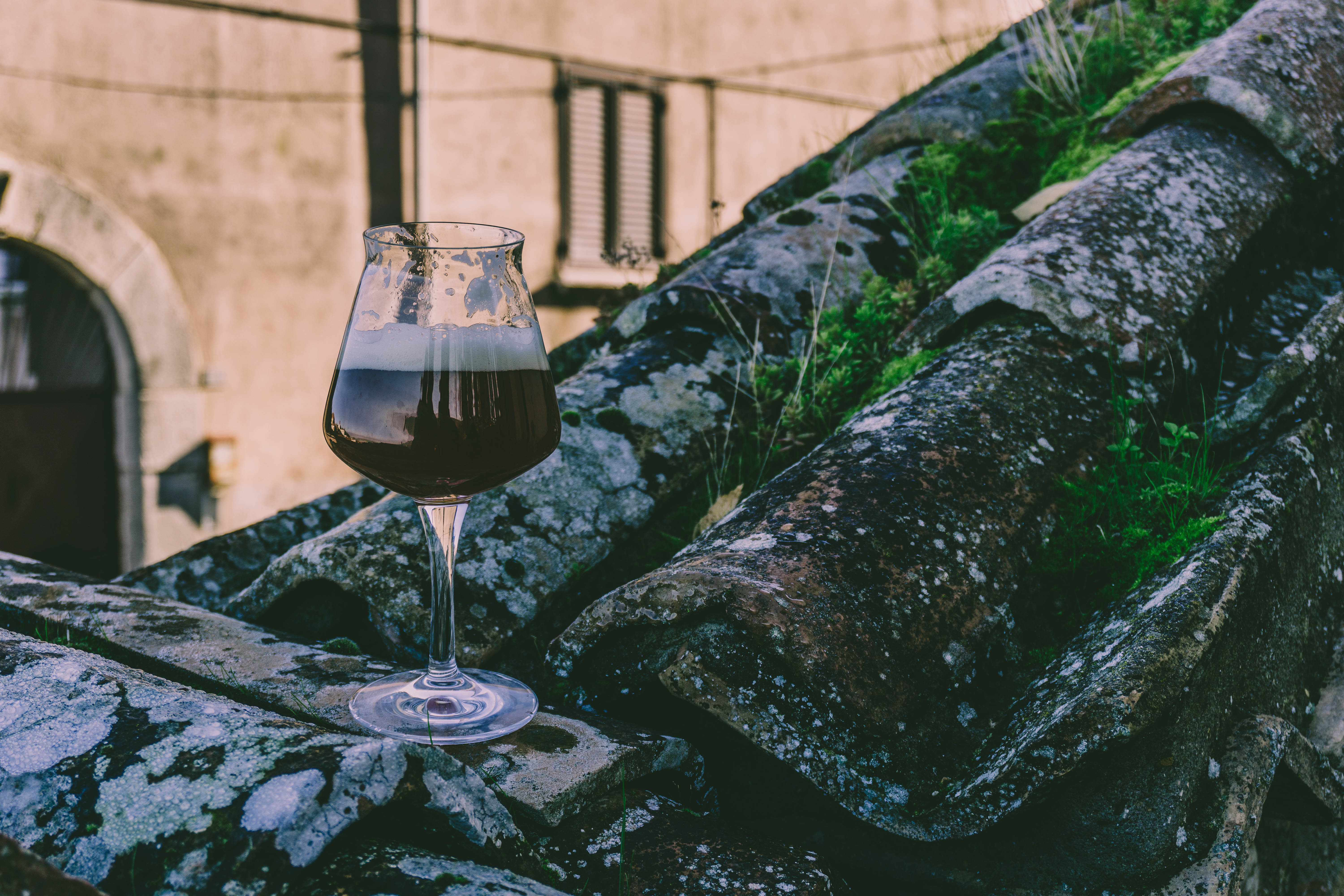 Calice di birra scura con schiuma su vecchie tegole di pietra ricoperte di muschio e licheni.