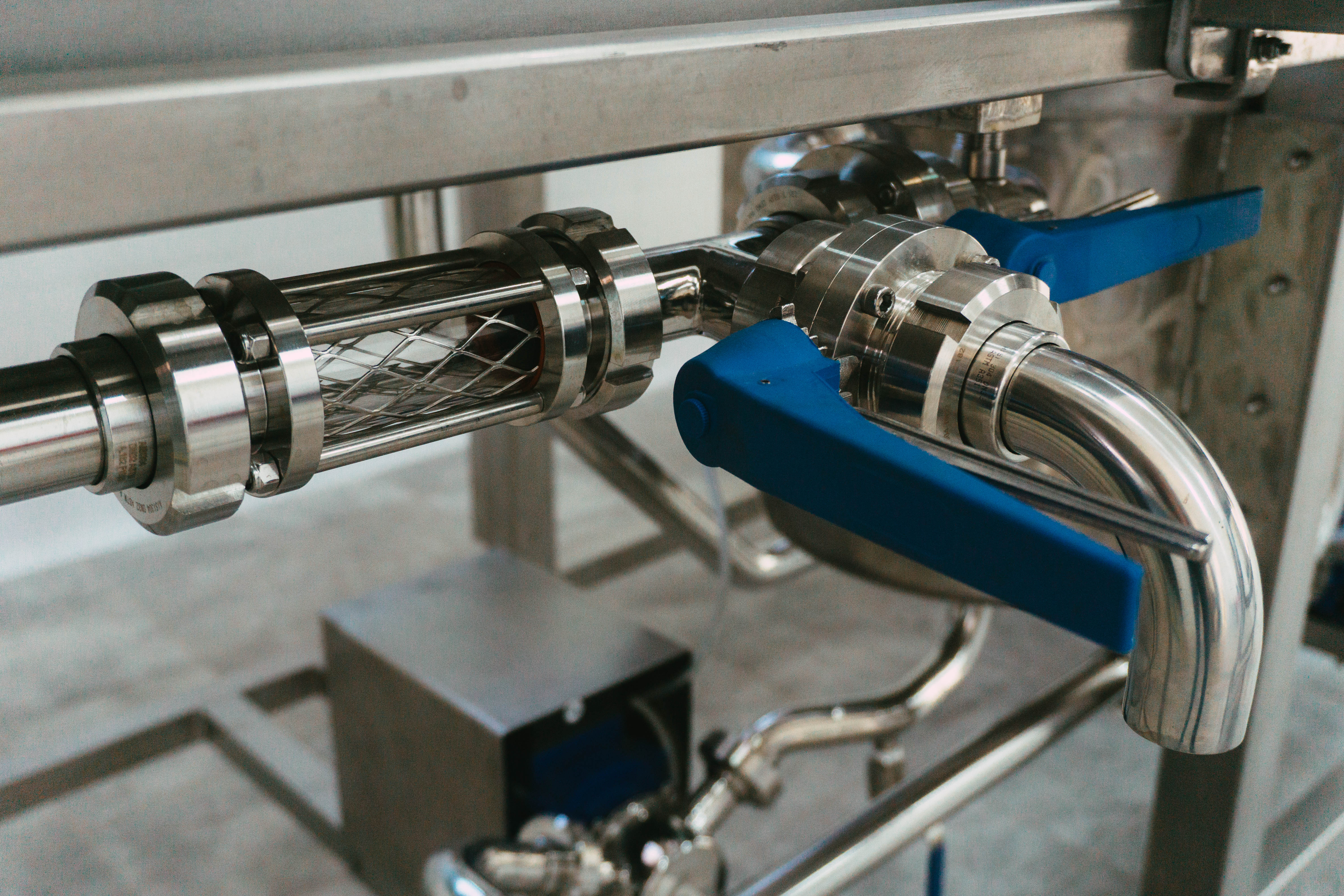Tubi e valvole in acciaio inossidabile con maniglie blu collegati a un sistema industriale.