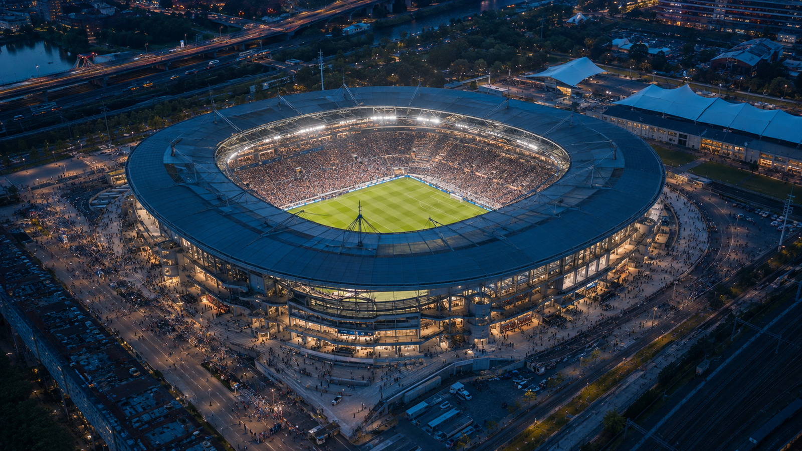 Overhead evening view of a full stadium, surrounding entrances, crowd approaches, and transport connections