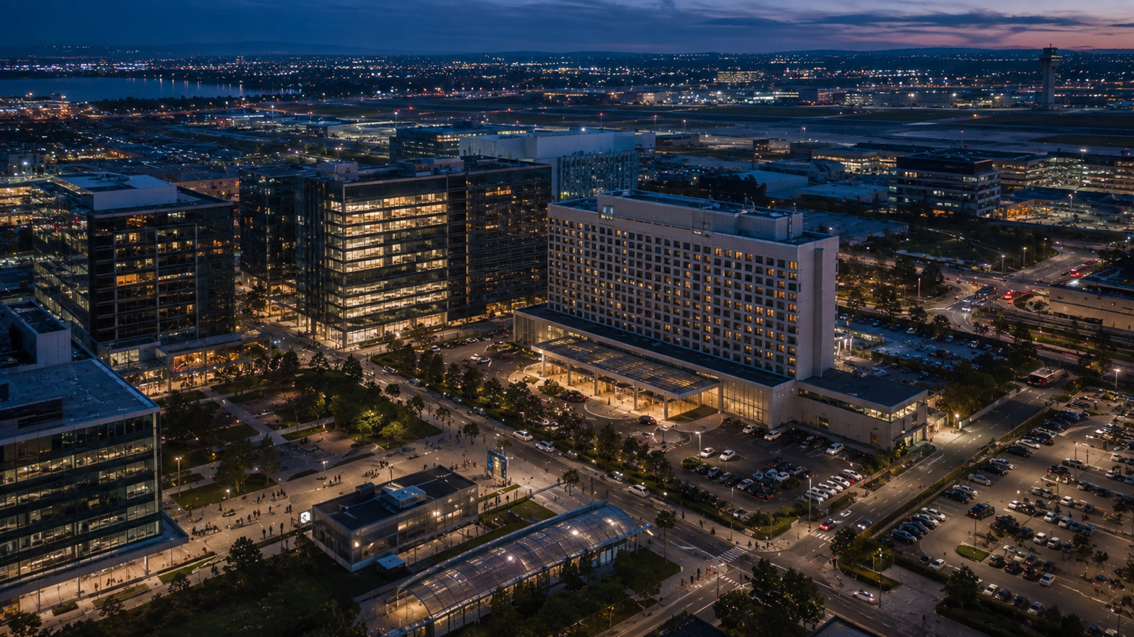 Aerial evening view of a business district, hotel, transport links, access points, and people moving between sites