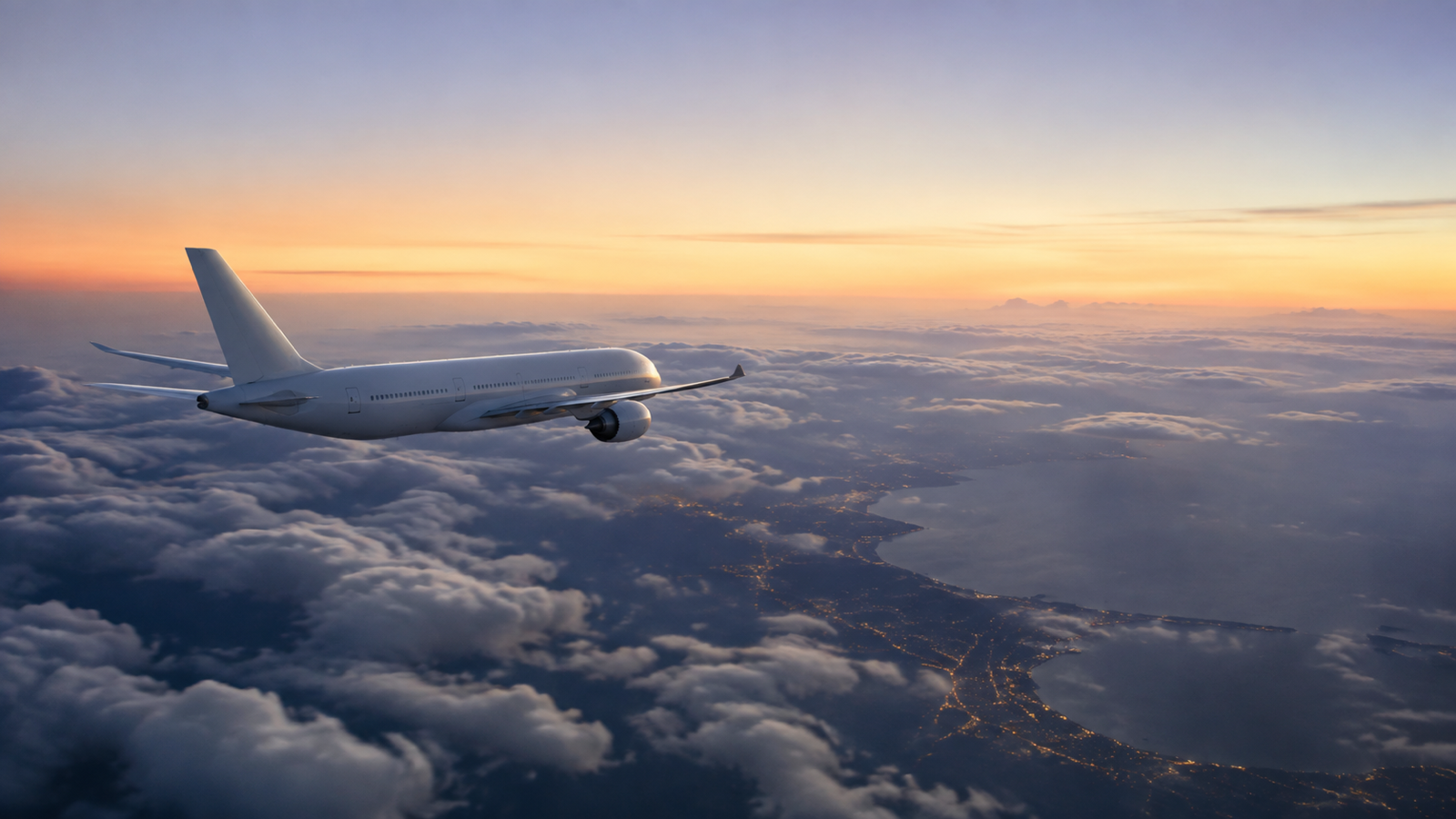 Passenger aircraft flying above clouds and a coastline at sunrise