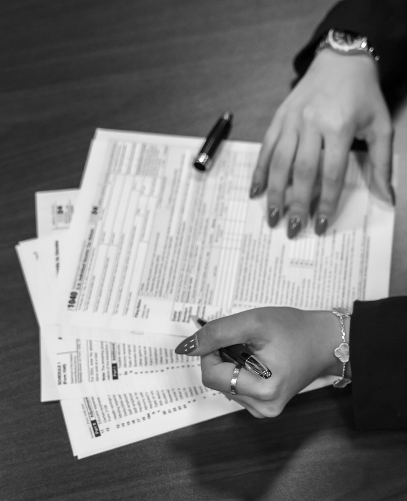 Person holding pen over a stack of tax forms on a wooden table.