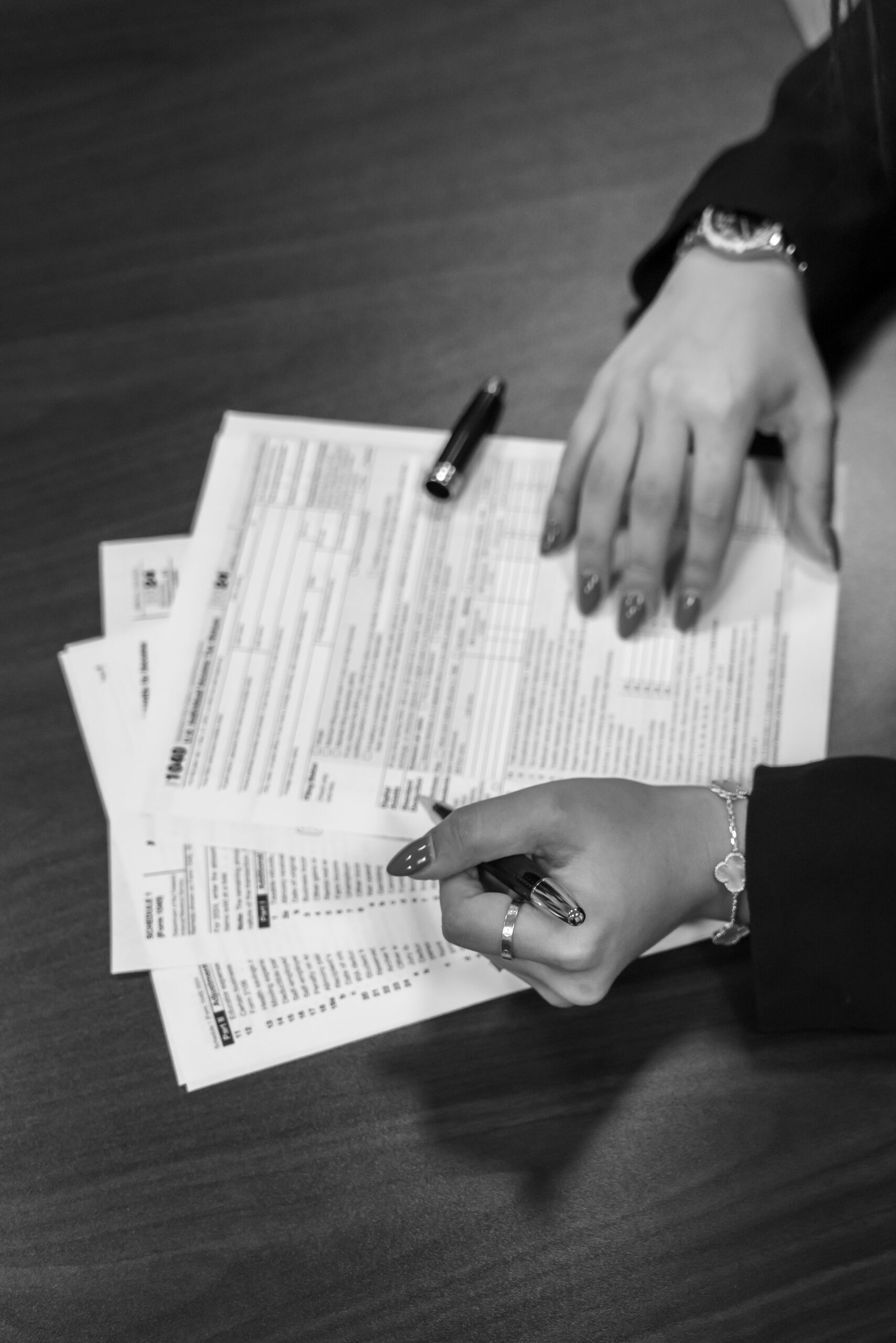 Hands holding and filling out tax forms with a pen on a wooden table.