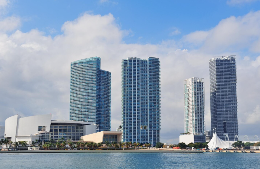 Waterfront view of modern Miami skyline featuring tall residential and commercial buildings under a partly cloudy sky.