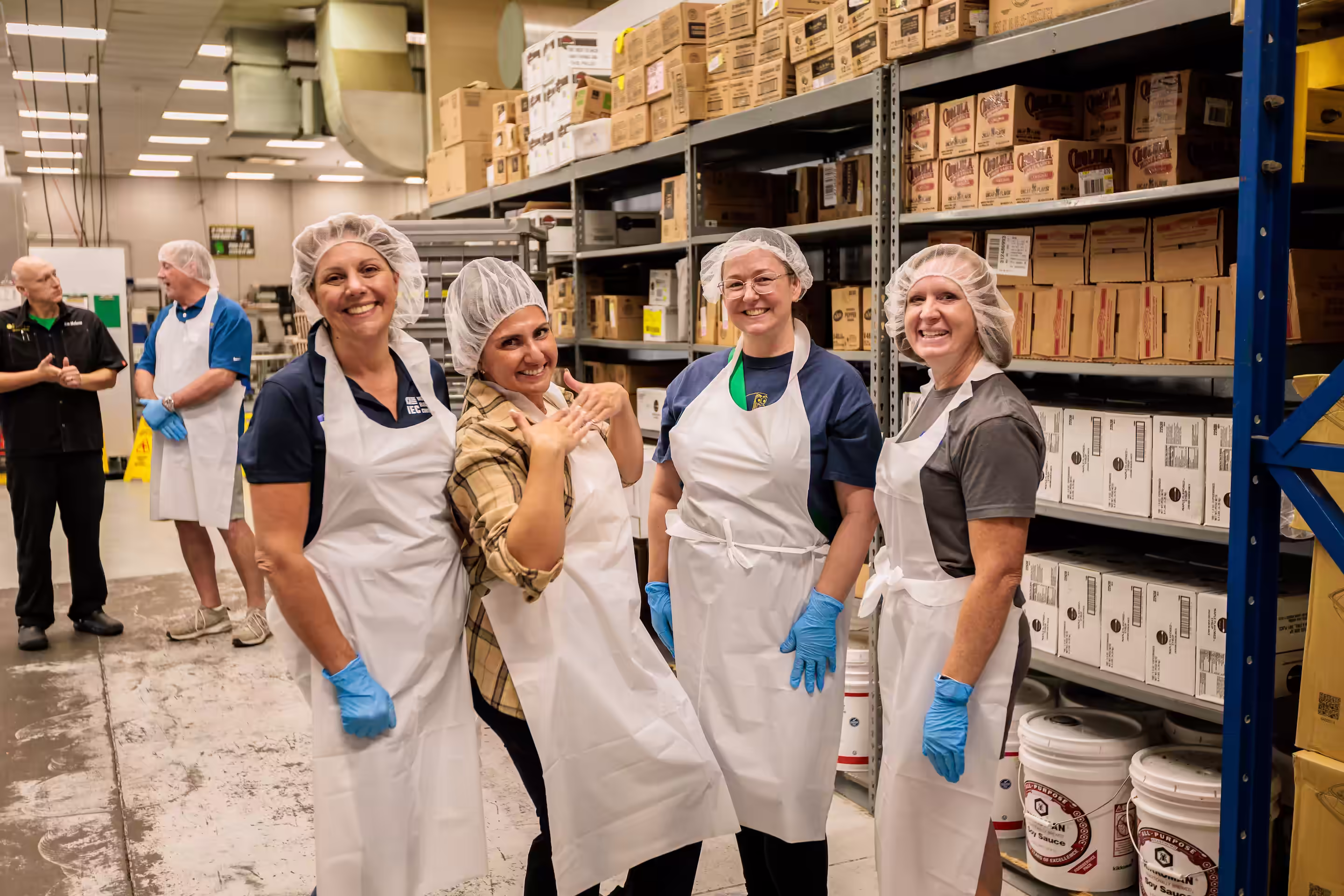 IEC Foundation members smiling in food safe gloves, hair nets, and aprons volunteering at St. Vincent DePaul
