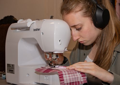 Karly sewing pink plaid fabric on a sewing machine