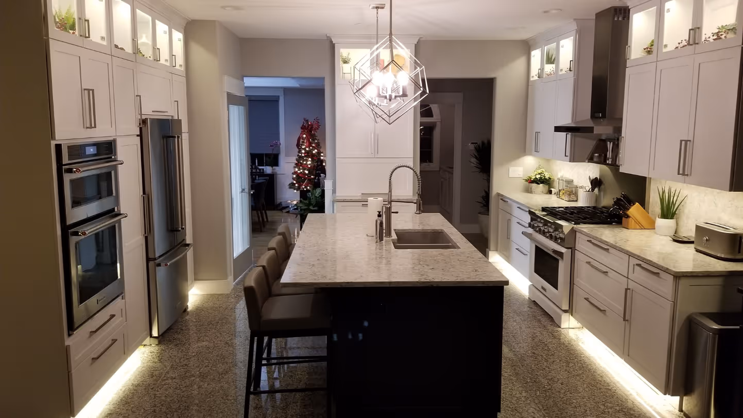 Modern kitchen with a large marble island, bar stools, stainless steel appliances, and a decorated Christmas tree in the adjoining room.