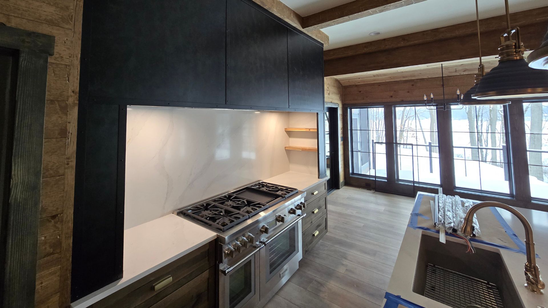 Modern kitchen with a large wooden island, stainless steel refrigerator, oven with striped towel, white cabinets, and pendant lights.