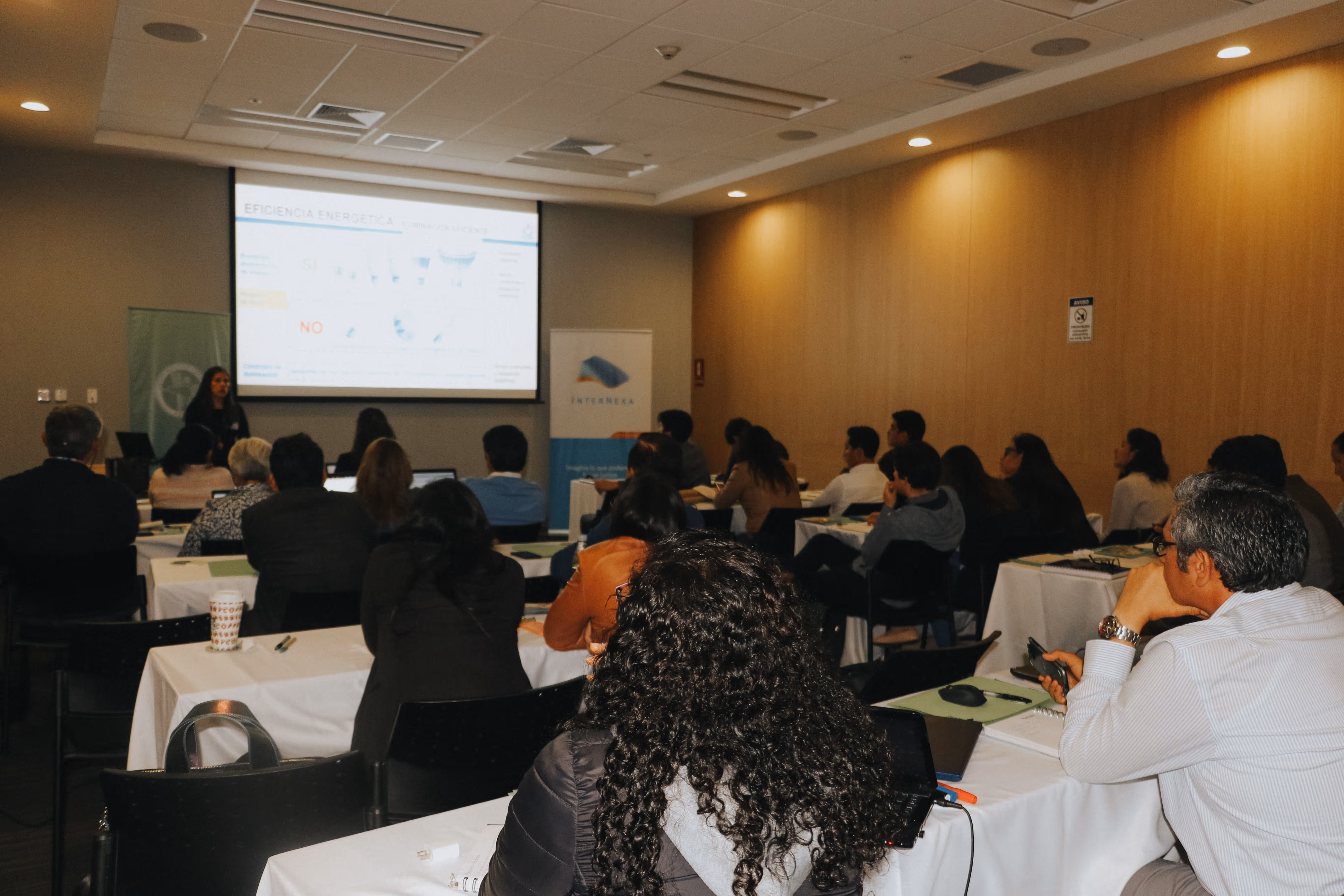 Grupo de personas en una sala de conferencias asistiendo a una presentación sobre eficiencia energética.
