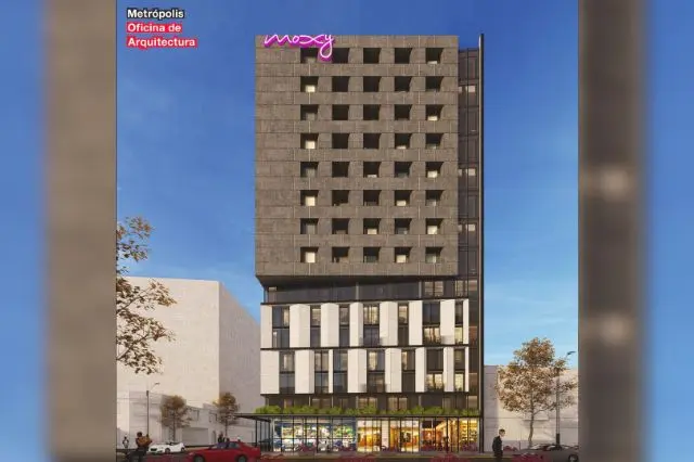 Edificio moderno de varios pisos con fachada con ventanas cuadradas pequeñas, cartel rosa de 'moxy' en la parte superior y árboles cerca de la entrada.