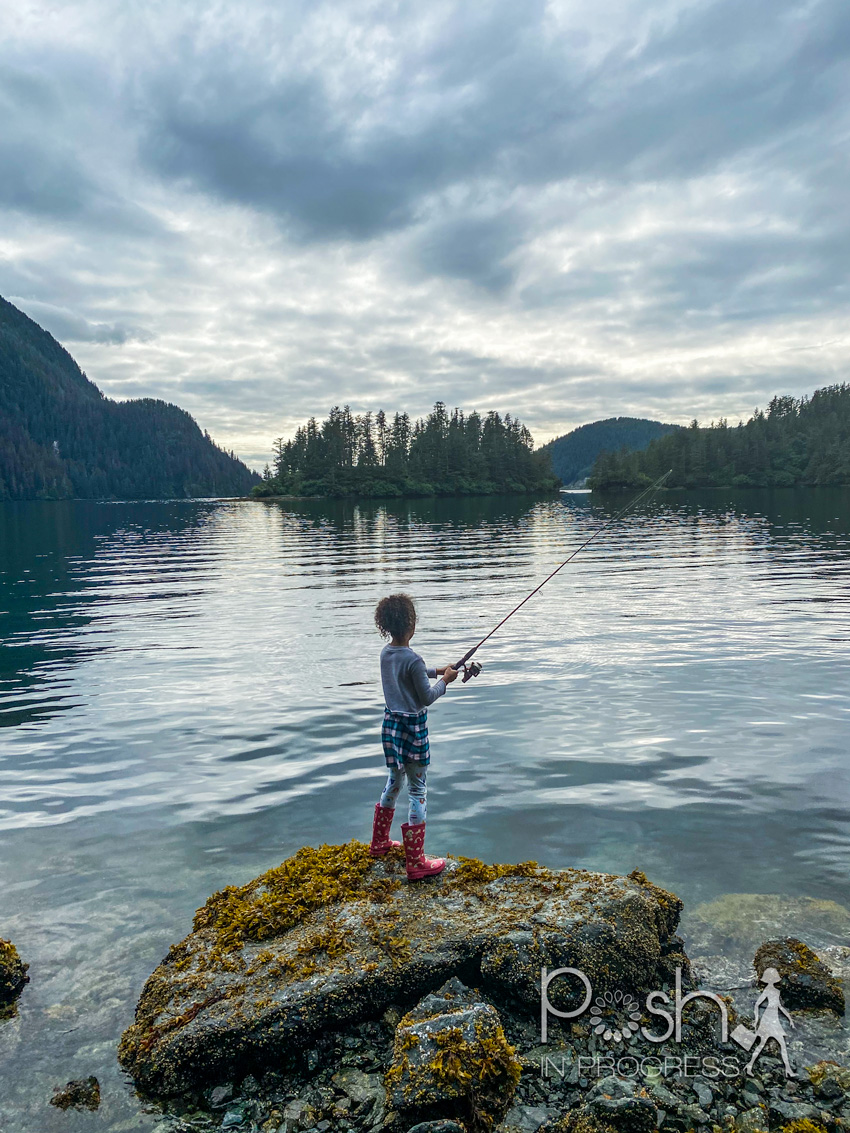 Things to do in Sitka Alaska by popular LA travel blog, Posh in Progress: image of a young girl standing on a rock and fishing. 