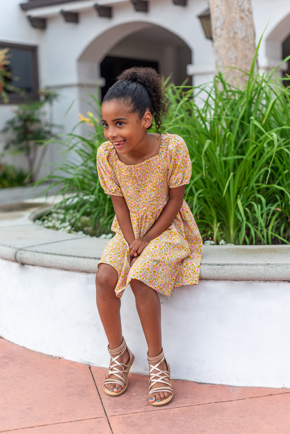 Mommy and Me Outfits by popular LA fashion blog, Posh in Progress: image of a young girl sitting outside and wearing a floral print dress and gold strap gladiator sandals. 