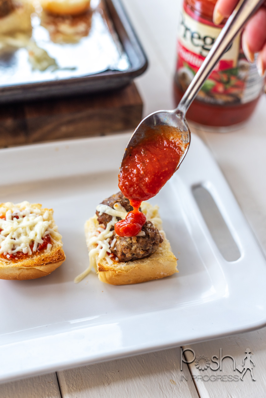 Meatball Sliders by popular LA lifestyle blog, Posh in Progress: image of a woman putting Prego spaghetti sauce on a meatball slider on a white rectangular ceramic tray.
