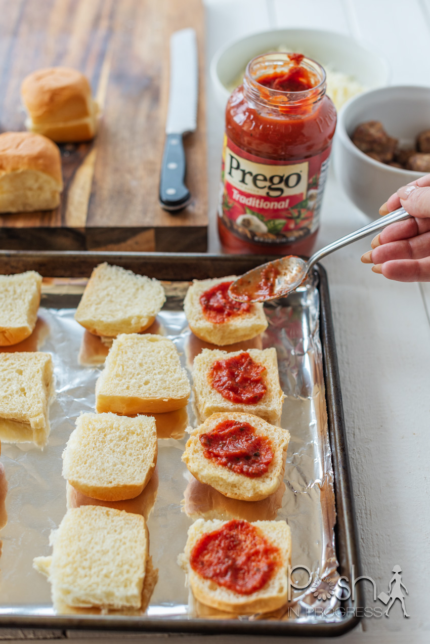 Meatball Sliders by popular LA lifestyle blog, Posh in Progress: image of a woman spreading Prego spaghetti sauce on rolls that have been placed on a baking sheet lined with tin foil.