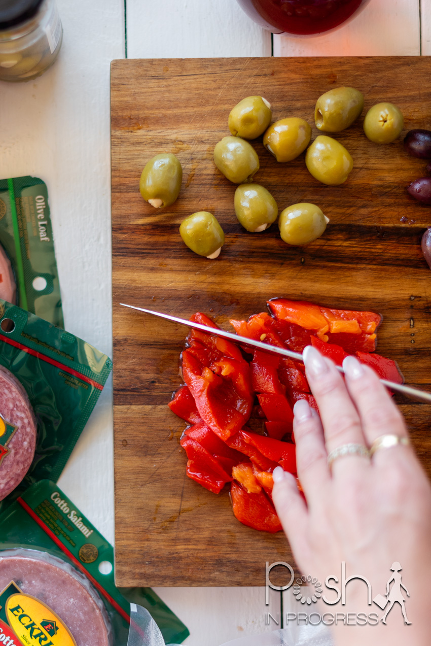 muffuletta-recipe-02 | Muffuletta Recipe by popular LA lifestyle blog, Posh in Progress: image of a woman cutting red peppers on a wooden cutting board next to some green olives. 