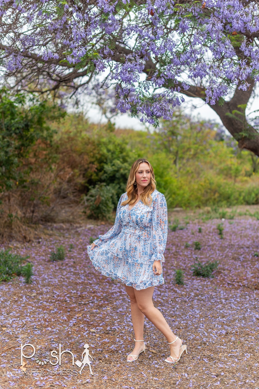 Backless Dresses by popular LA fashion blog, Posh in Progress: image of a woman standing under a jacaranda tree and wearing a white floral print dress with white heel sandals. 