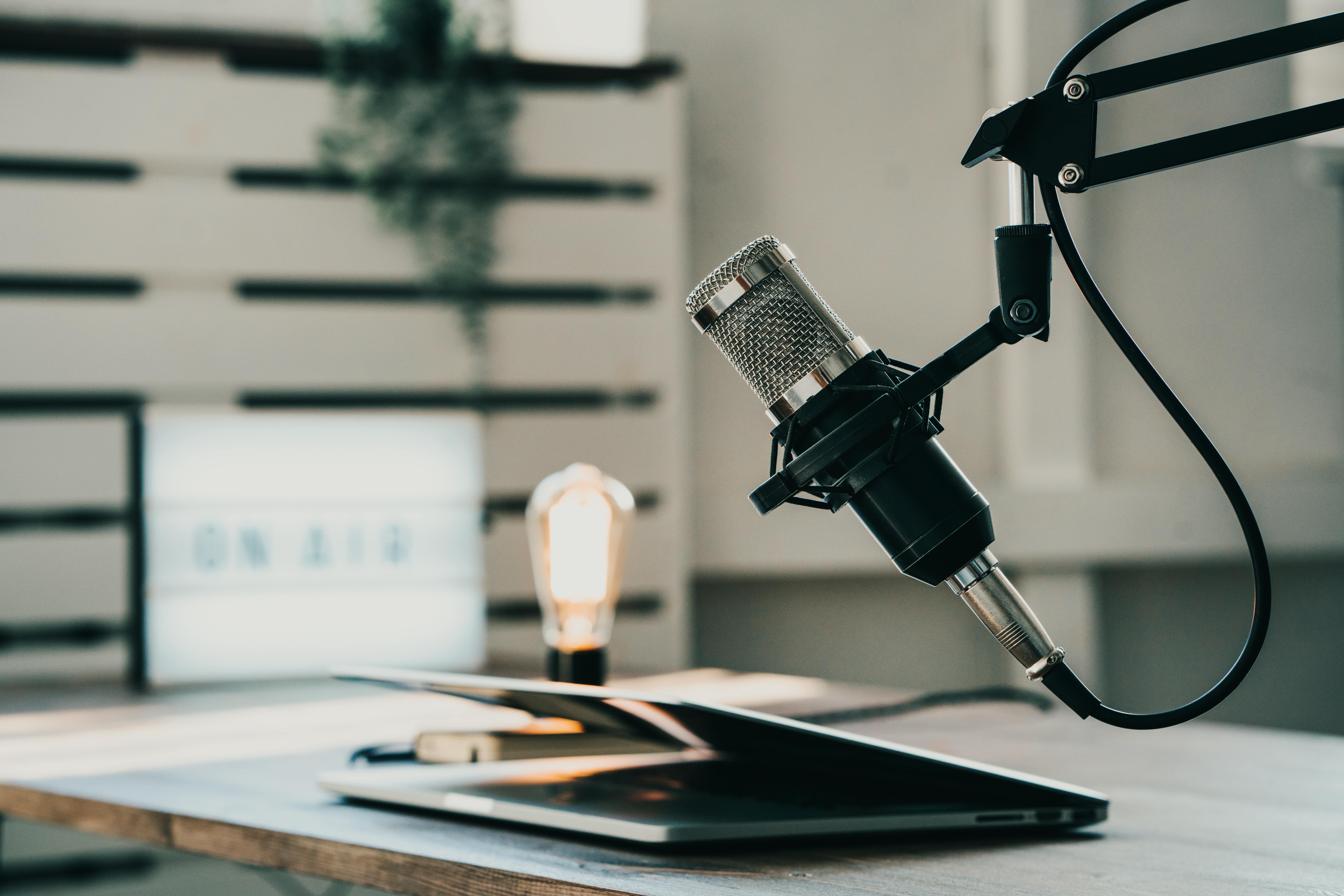 A close-up, professional photograph of a silver studio microphone on a boom arm, set up in a recording booth. To the right is a form titled "Want to be a Guest on Our Podcast?"